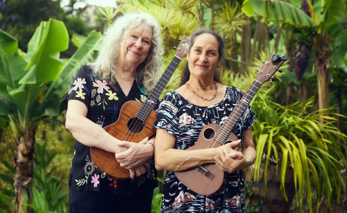 The Hula Honeys With Their Ukuleles Standing In Front Of Tropical Greenery