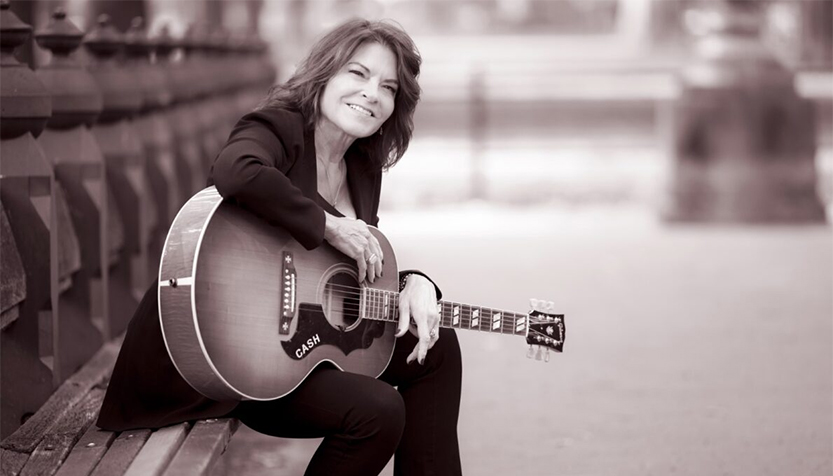 Rosanne Cash Sitting On A Park Bench With Her Guitar