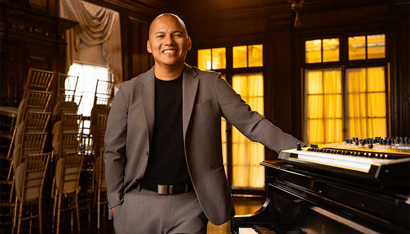 Chris Hon In A Gray Suit Smiling And Standing By The Piano