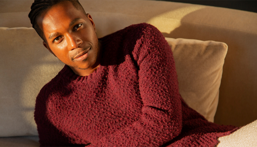 Leslie Odom Jr. In A Maroon Sweater Reclining On A Couch