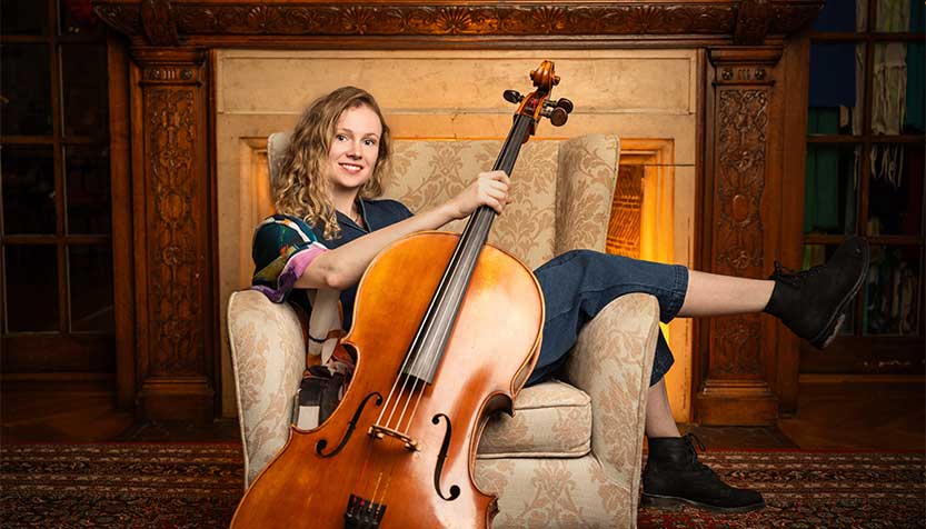 Ellen Gira Lounging In A Chair Holding Her Cello By The Neck