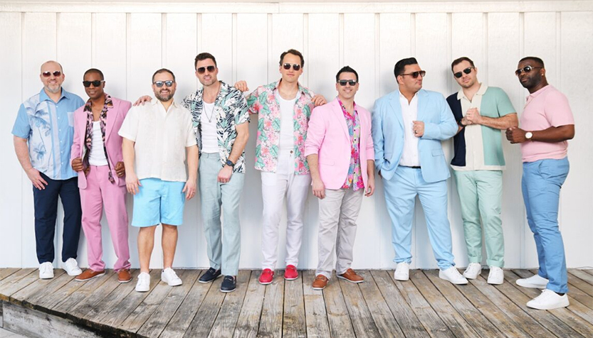 Straight No Chaser Members In Casual Attire Against A White Building