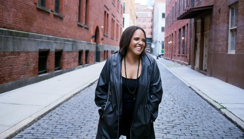Terri Lyne Carrington In A Black Leather Jacket Smiling In The Middle Of A Brick Street