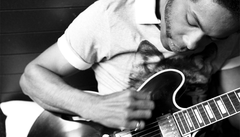 Alex Cuba Leaning Over While Playing Guitar