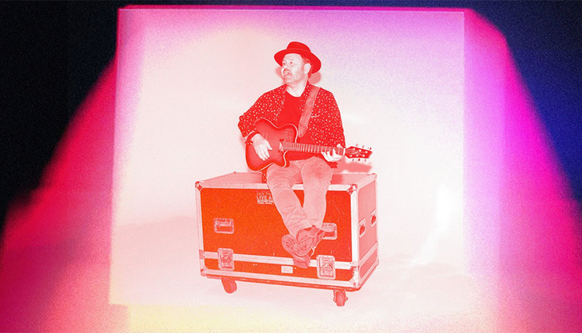Martin Sexton Sitting On A Box Holding A Guitar