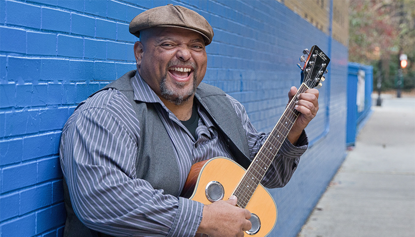 Kevin Burt With Guitar In Front Of Blue Wall