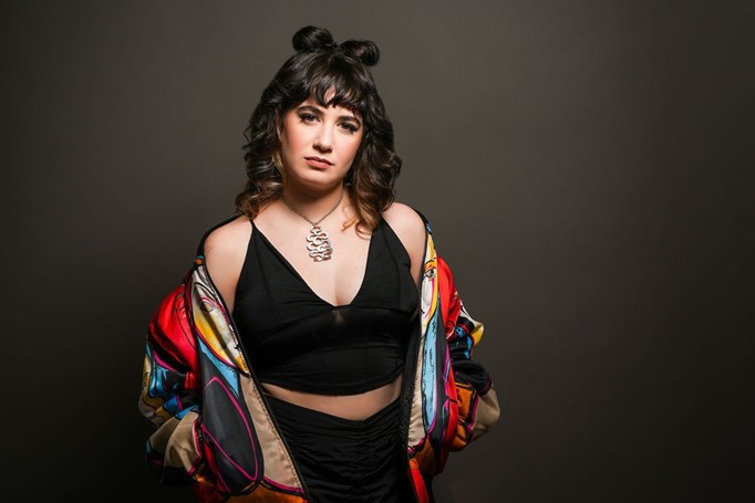 Alex Hamburger wearing a blank tank, colorful jacket, and a space buns hairstyle