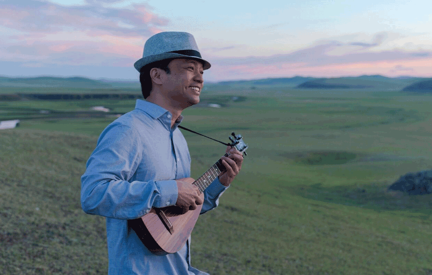 Dan Ho Wearing A Fedora And Playing His Uke In A Field