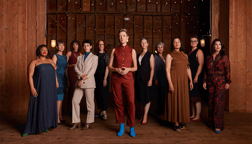 Lorelei Ensemble Members Standing In A Barn With String Lights Behind Them