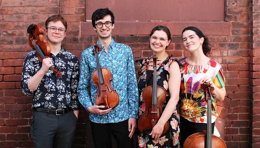Argus Quartet Standing In Front Of A Brick Wall With Their Instruments