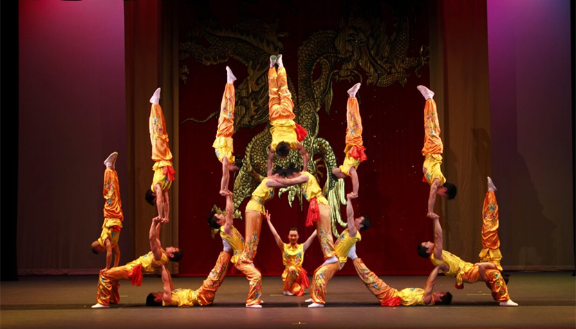 Peking Acrobats In Red And Gold Costumes Performing A Balancing Act