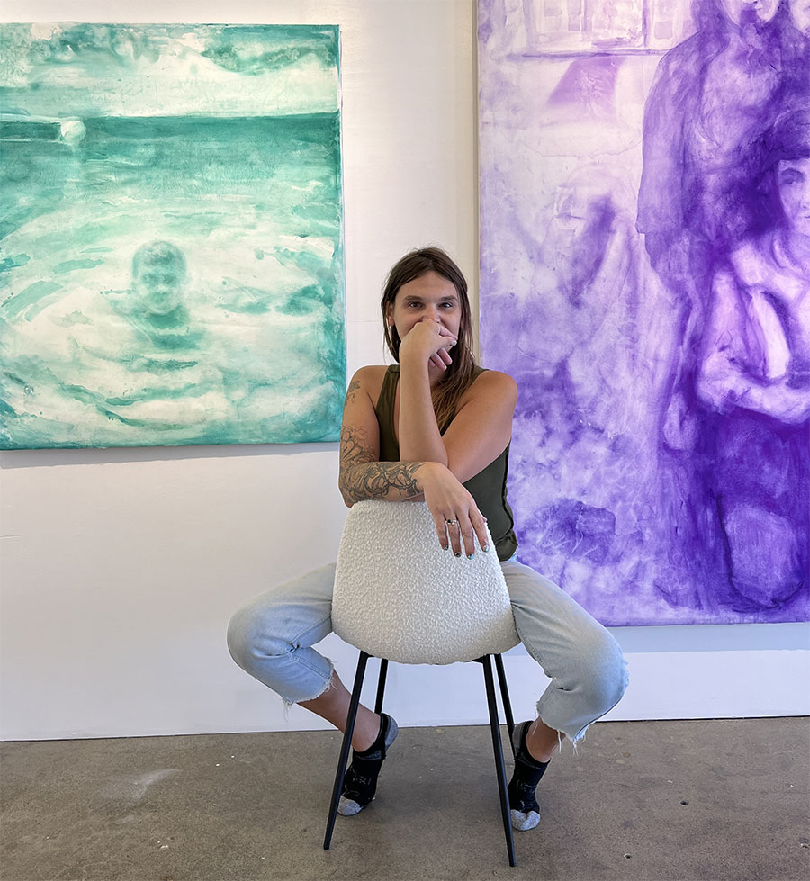 Breanna Cee Martins Sitting Backward On A Chair In Front Of Her Paintings