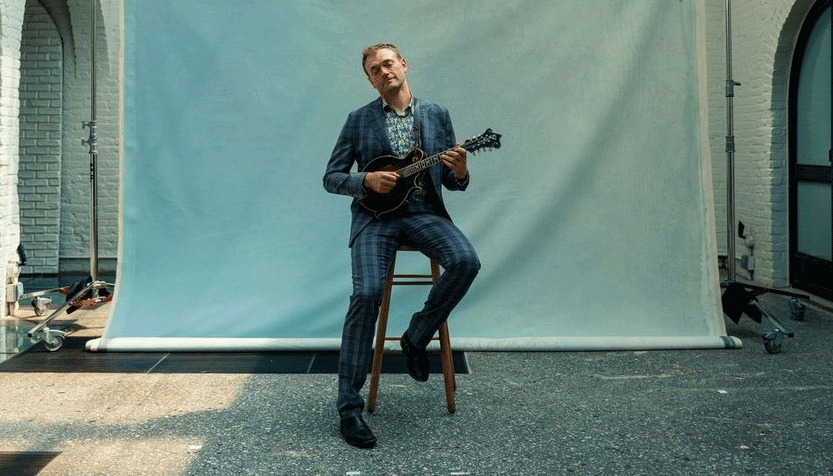 Chris Thile In A Blue Plaid Suit Sitting On A Stool Outside