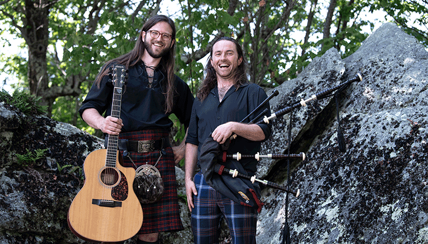 Kevin And Jesse Wearing Plaid In A Forest Holding Their Instruments And Smiling